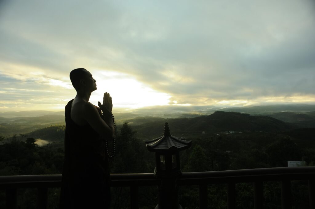 pexels-photo-2730217-2730217 A monk in silhouette prays peacefully at sunrise with mountains in the background.